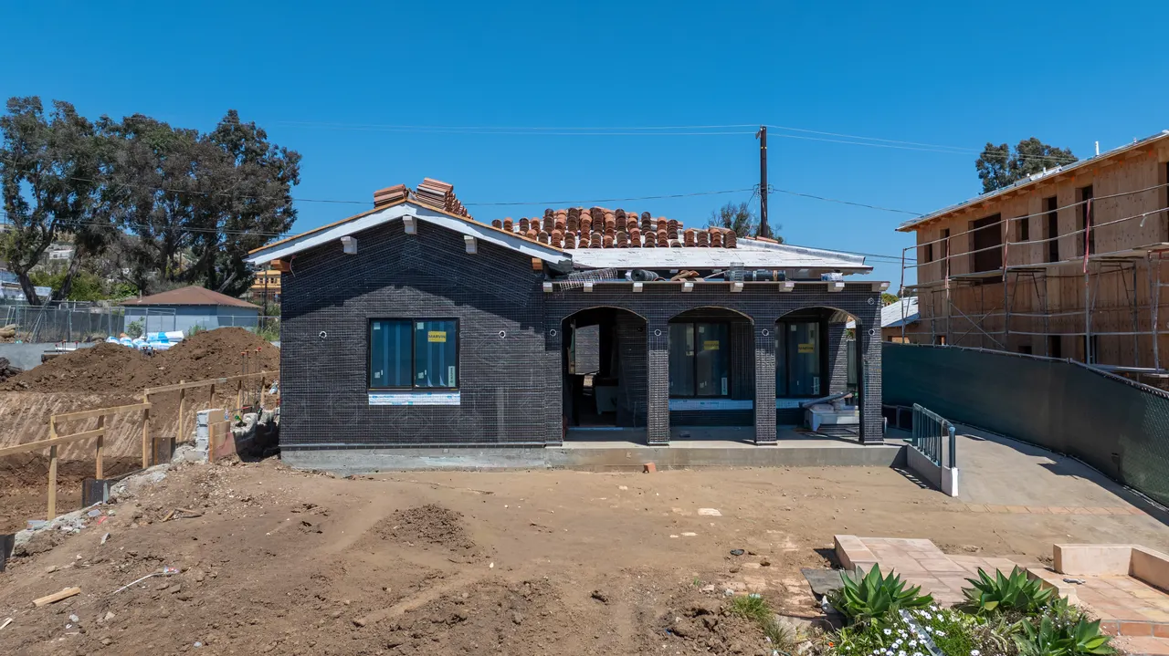 Aerial close-up of the home's arched covered entry and gabled roofline with clay roof tiles installed, surrounded by bare dirt yard