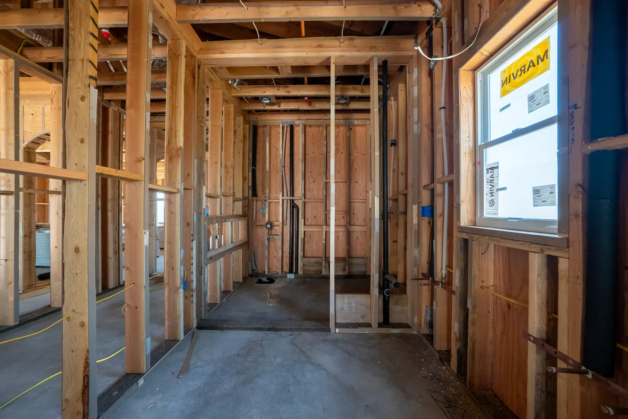 Framed bathroom with rough plumbing valves and drain lines for a shower and fixtures, stud walls not yet insulated