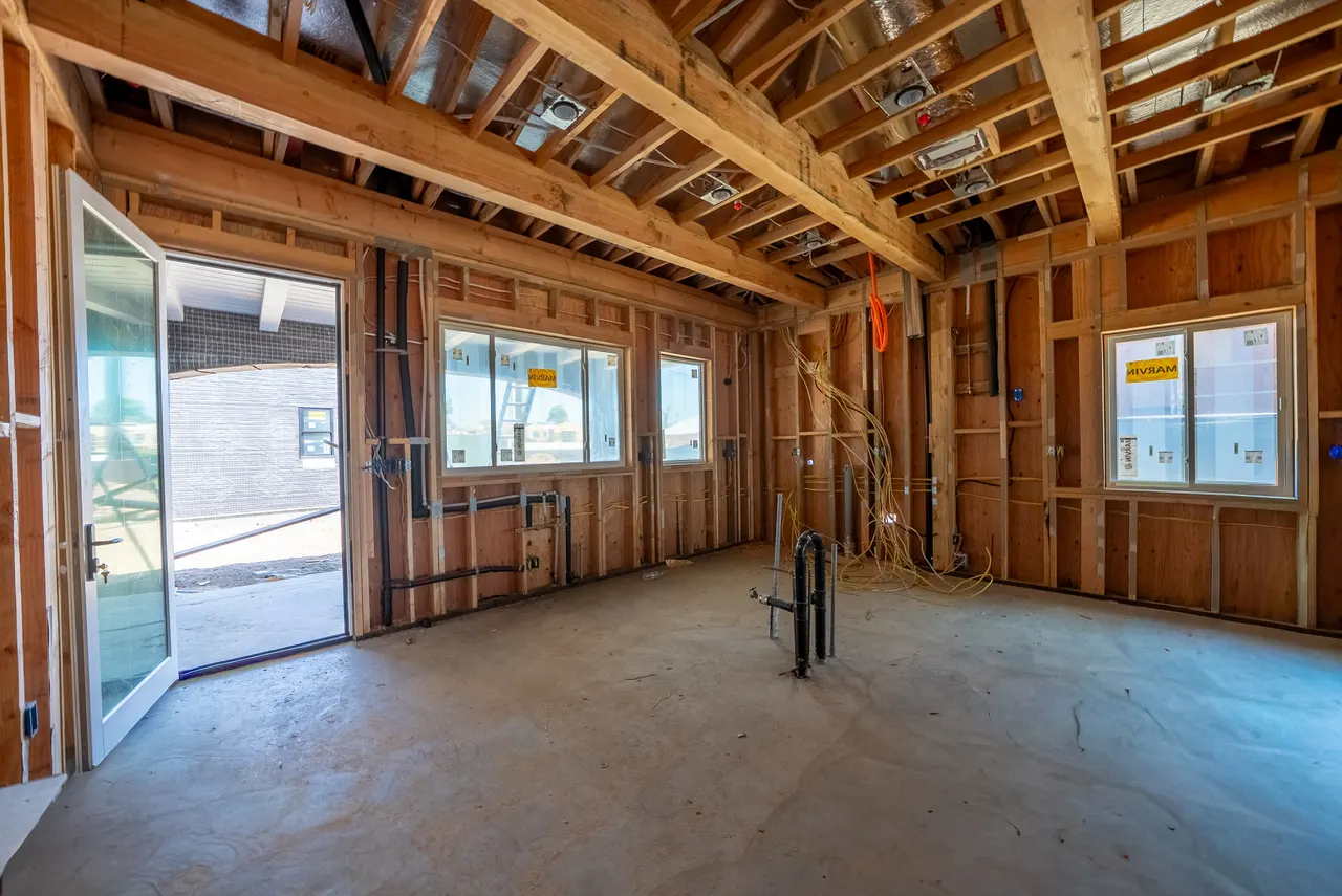 Framed bedroom with a vaulted ceiling, corner windows, a sliding glass door to the yard, and rough plumbing stub-outs in the concrete floor