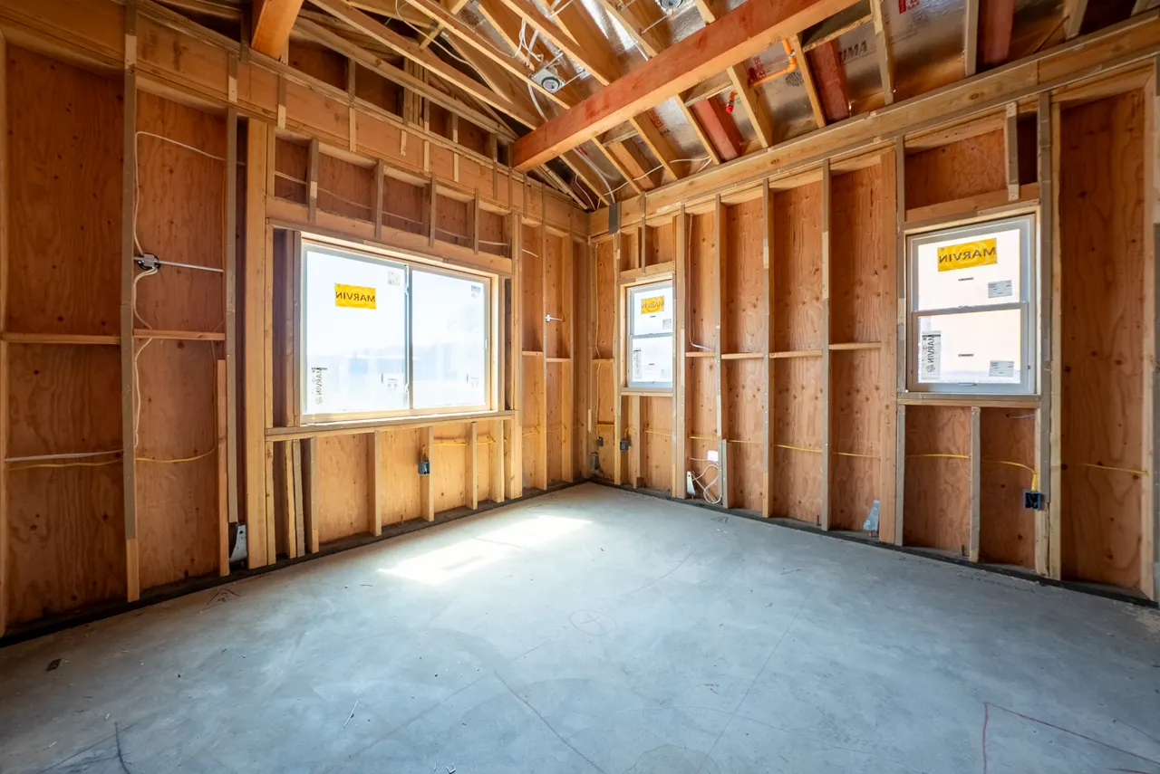 Framed bedroom with a vaulted ceiling and three windows bringing in natural light, concrete slab floor
