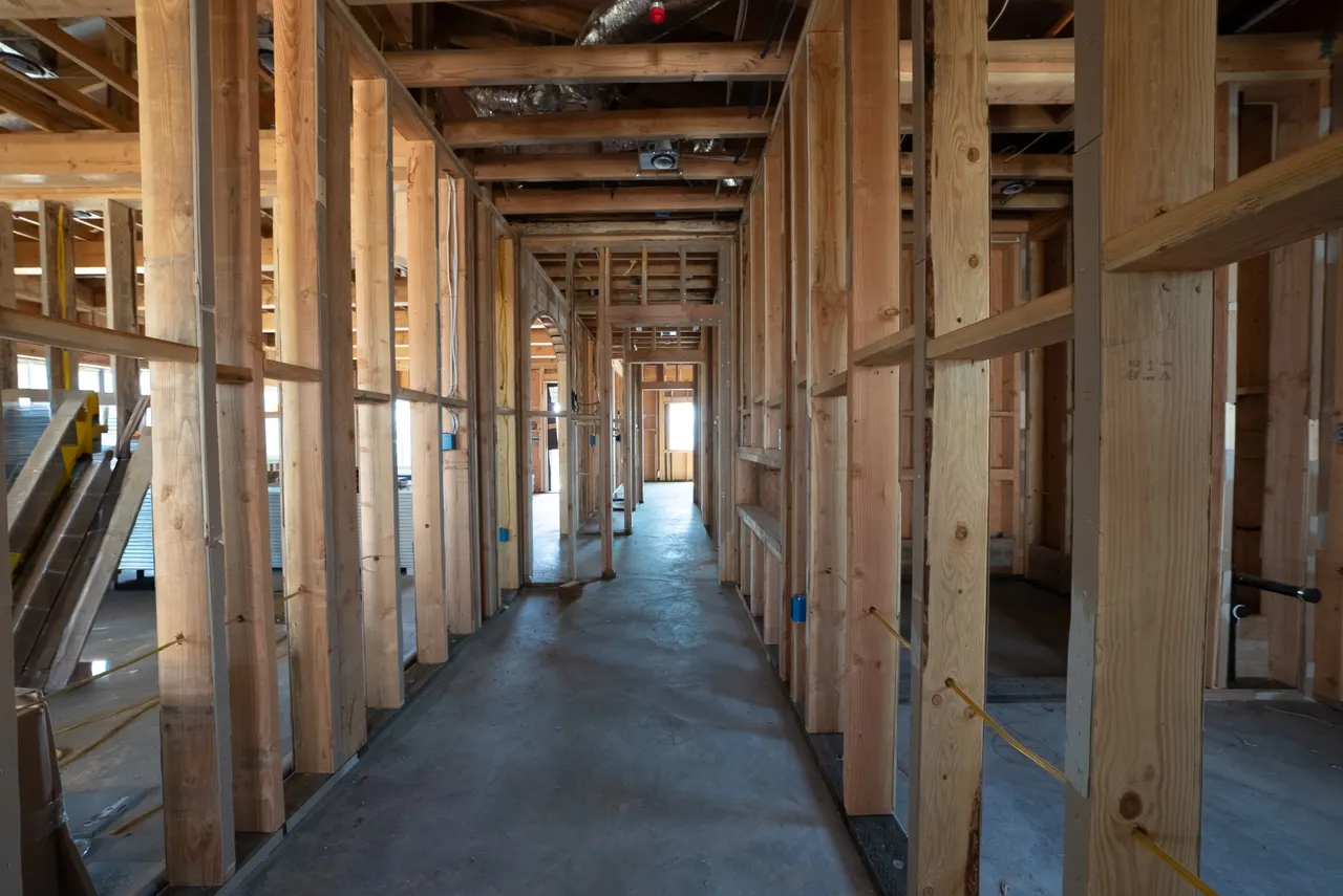 Framed hallway lined with stud walls leading toward an arched doorway at the far end
