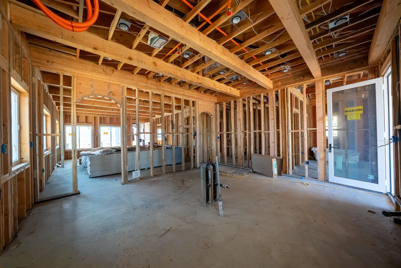 Framed open kitchen and living area with an arched doorway, a rough plumbing stub-out in the floor, and a glass door to the exterior
