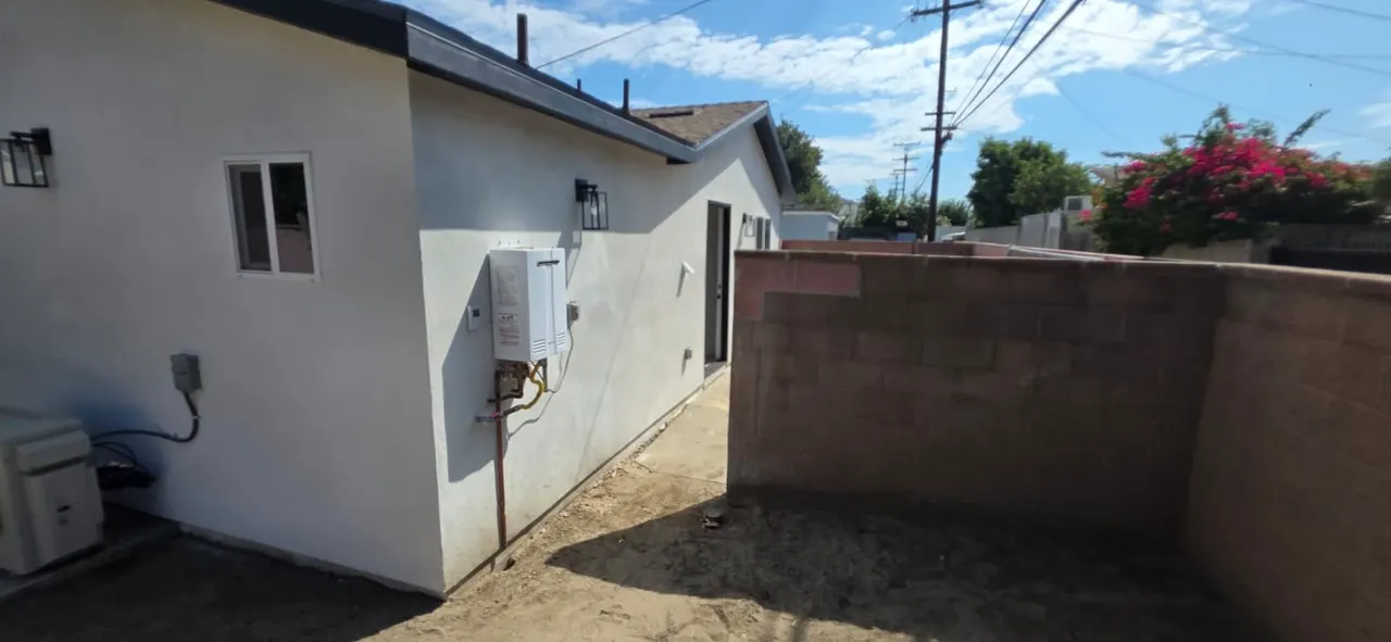 Tankless water heater and gas line connections mounted on the ADU's exterior stucco wall, with an electrical panel below
