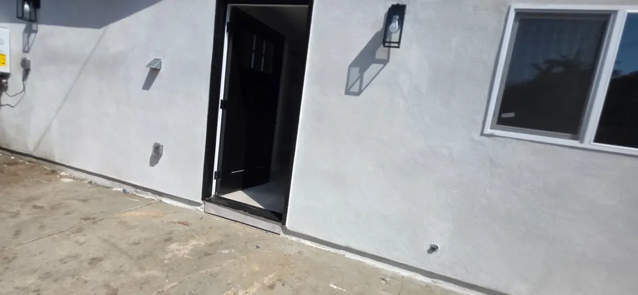 Close-up of a black exterior door and window trim against the ADU's white stucco wall with a wall sconce light fixture
