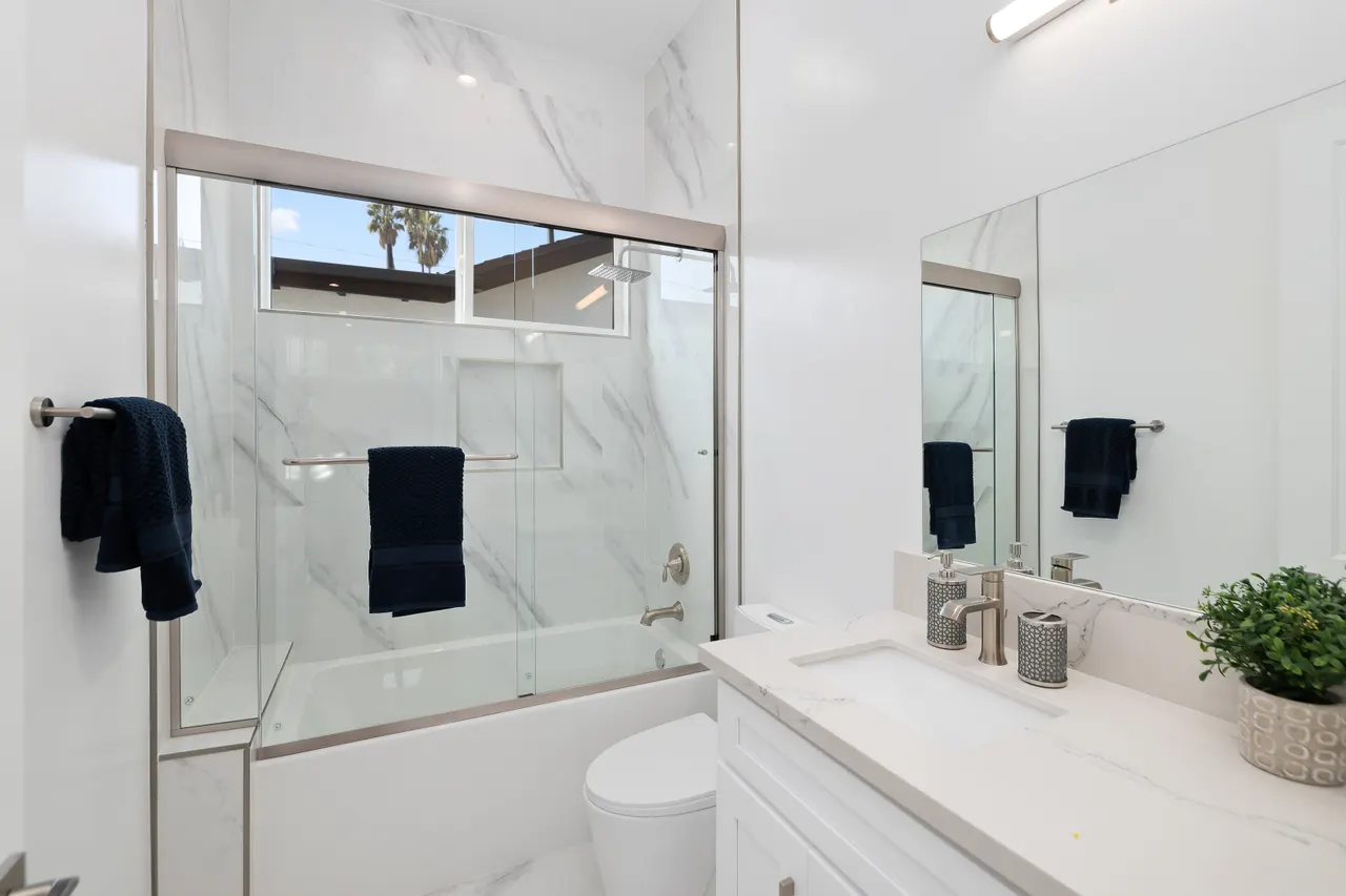 Bathroom with a glass-enclosed shower and tub combo, marble tile walls, black towels, and a white vanity with mirror