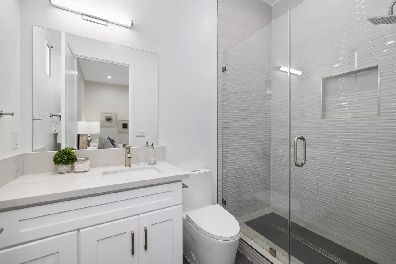Bathroom with a frameless glass shower stall, marble tile flooring and walls, and a white vanity with mirror