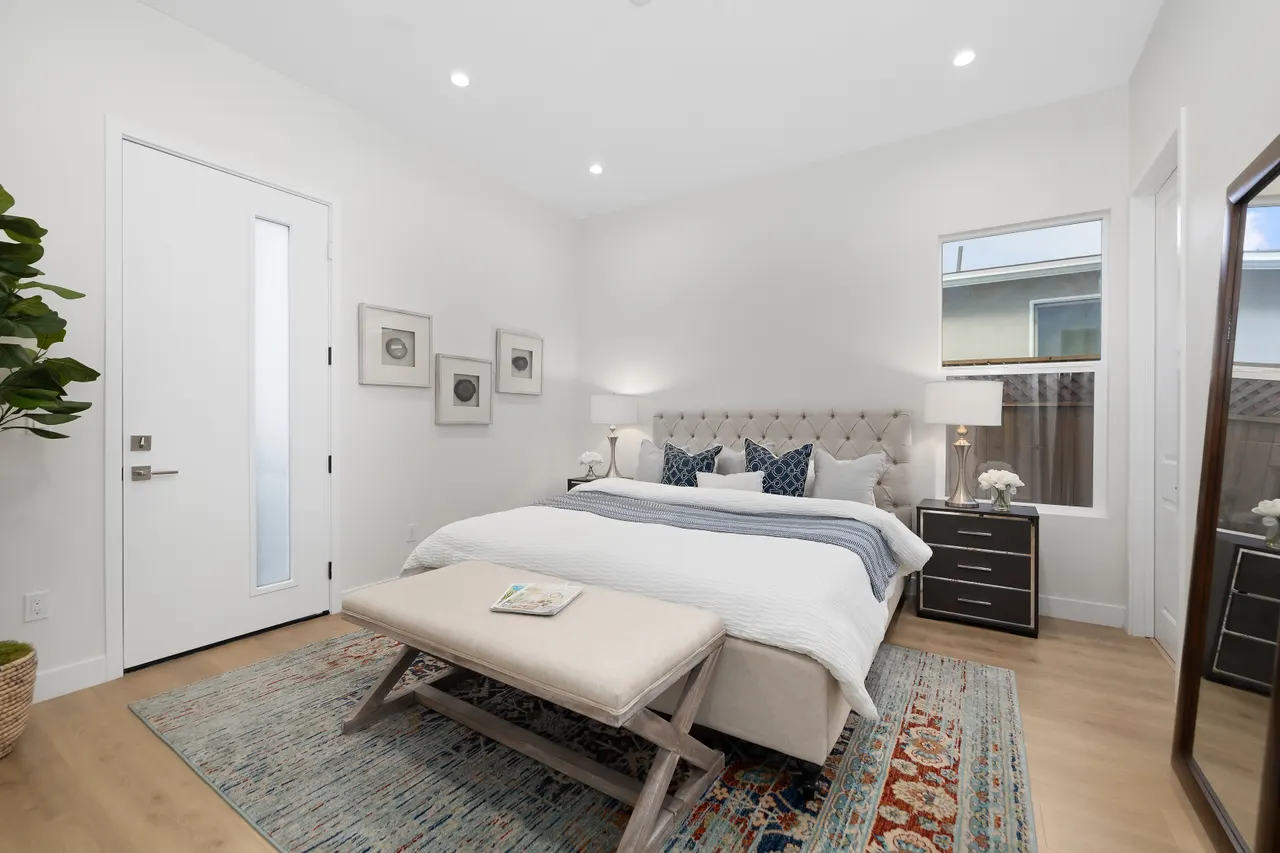 Primary bedroom with a beige tufted upholstered headboard, white bedding with navy accent pillows, a wood bench at the foot of the bed, and a mirror