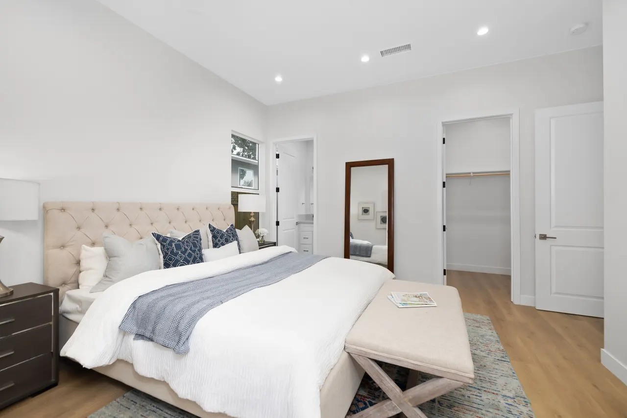 Bedroom wide view with a tufted headboard, bench, floor mirror, closet door, and light wood flooring