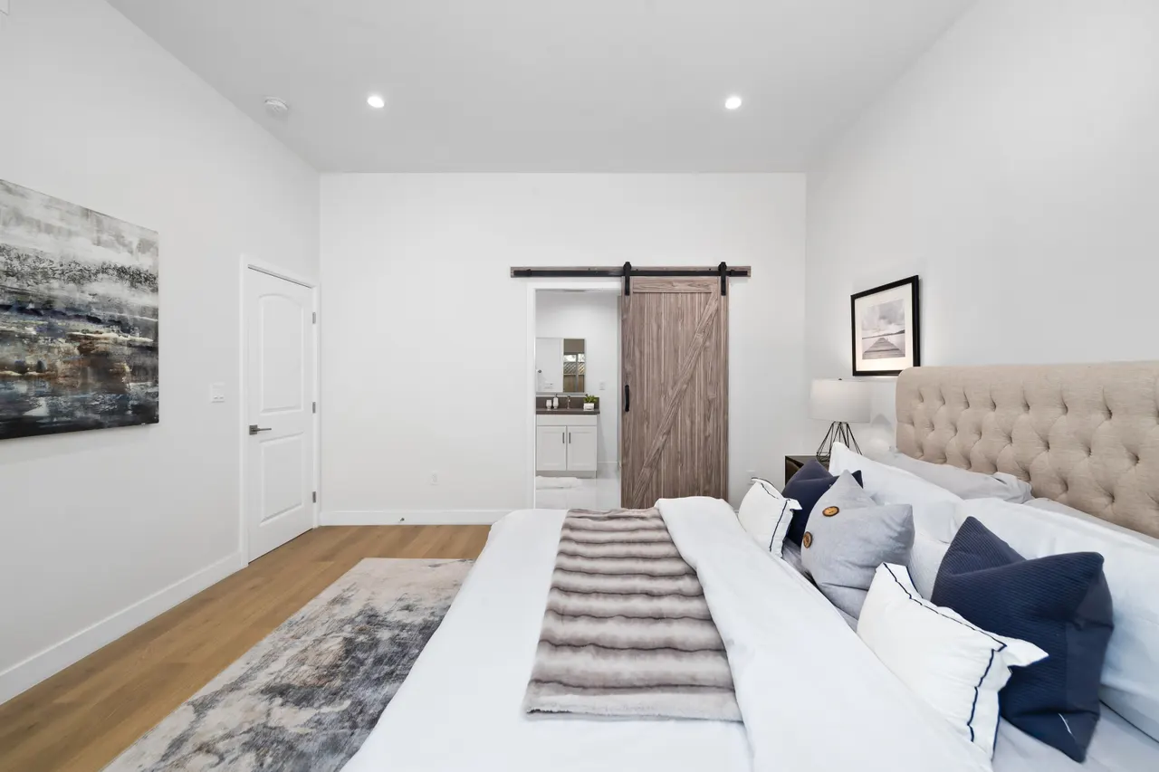 Bedroom with a tufted upholstered headboard, a sliding barn door to the closet, framed art above the bed, and a window