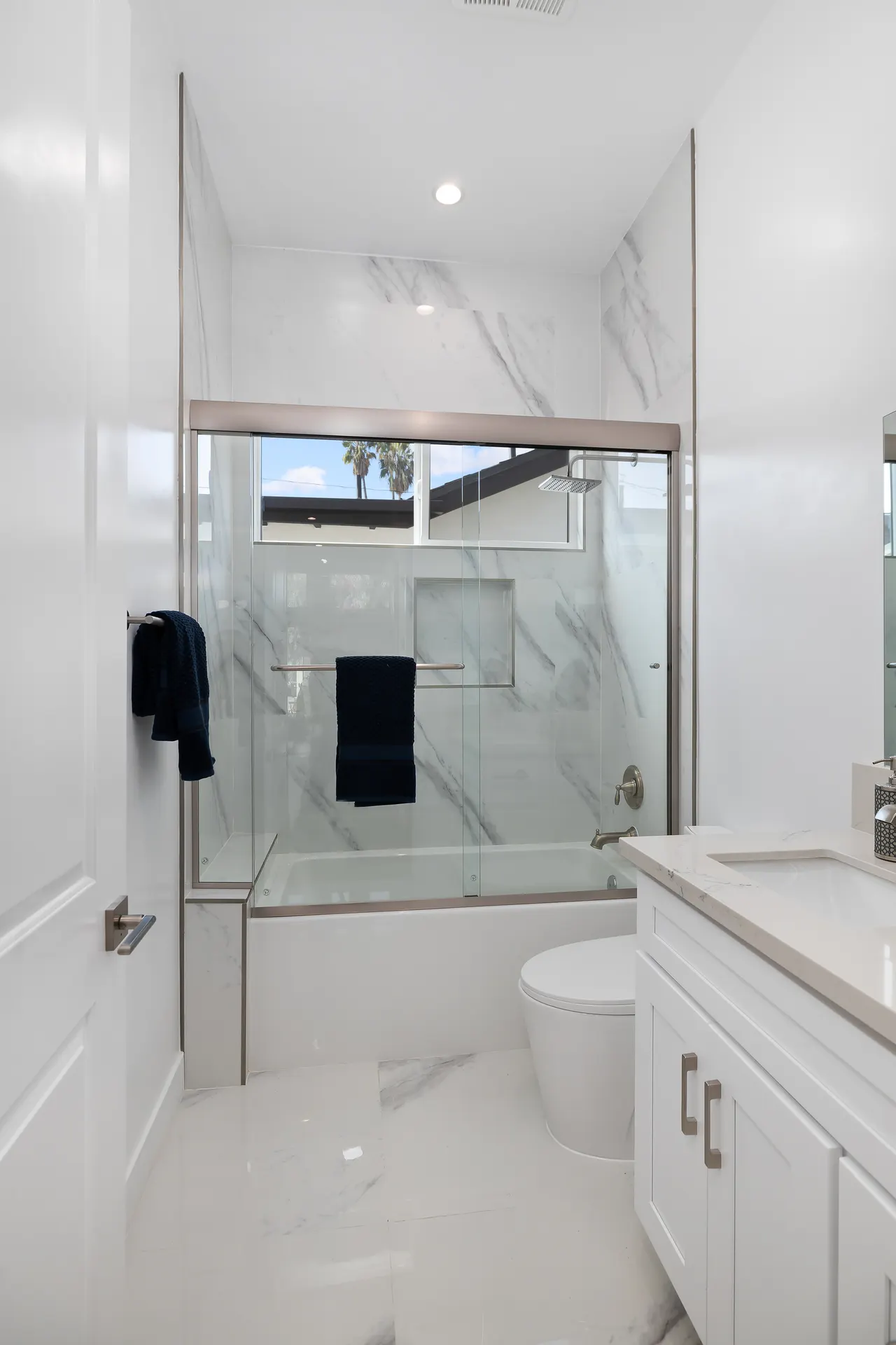 Primary bathroom with a freestanding soaking tub beside a glass-enclosed shower, full marble slab walls, and a white vanity
