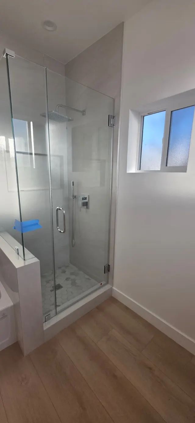 Detail of a frameless glass shower with a rainfall showerhead and hexagon tile floor