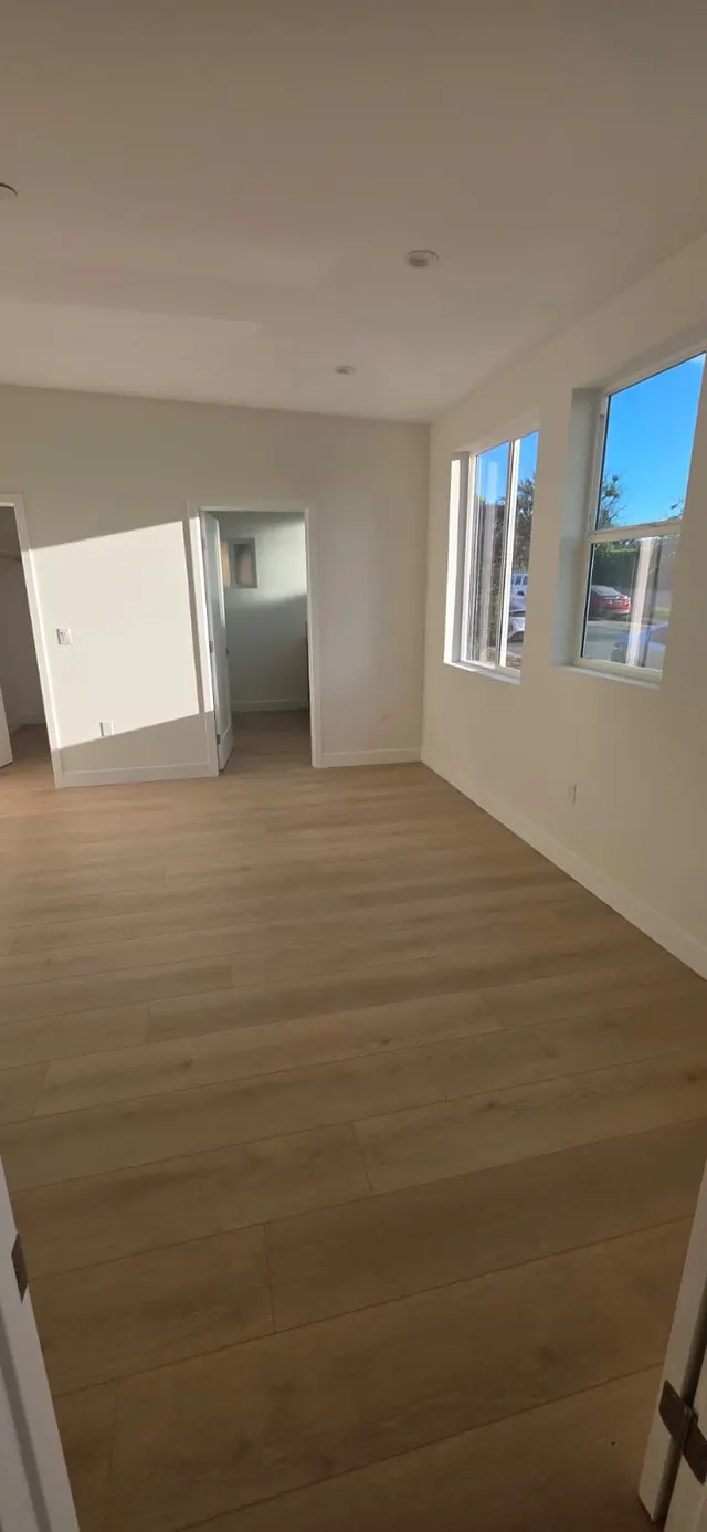 Bright bedroom corner with two windows, wood-look flooring, and a closet doorway