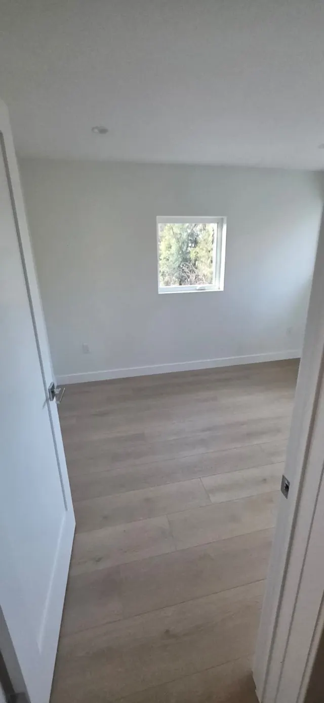 Bedroom with a single window overlooking trees and wood-look flooring