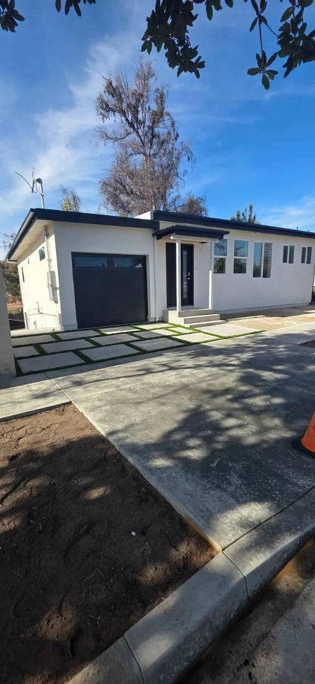 Front elevation of the home showing white stucco siding, black-framed windows, and the entry walkway