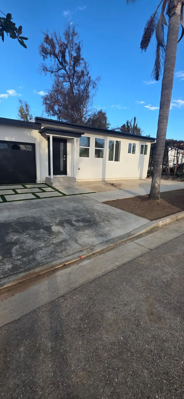 Close view of the front entry with navy door, concrete steps, and paver-and-turf walkway