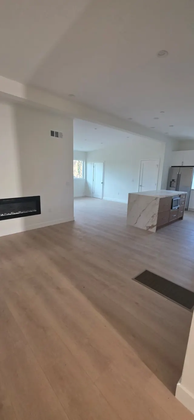 Open great room with a wall-mounted linear fireplace and a sightline into the kitchen
