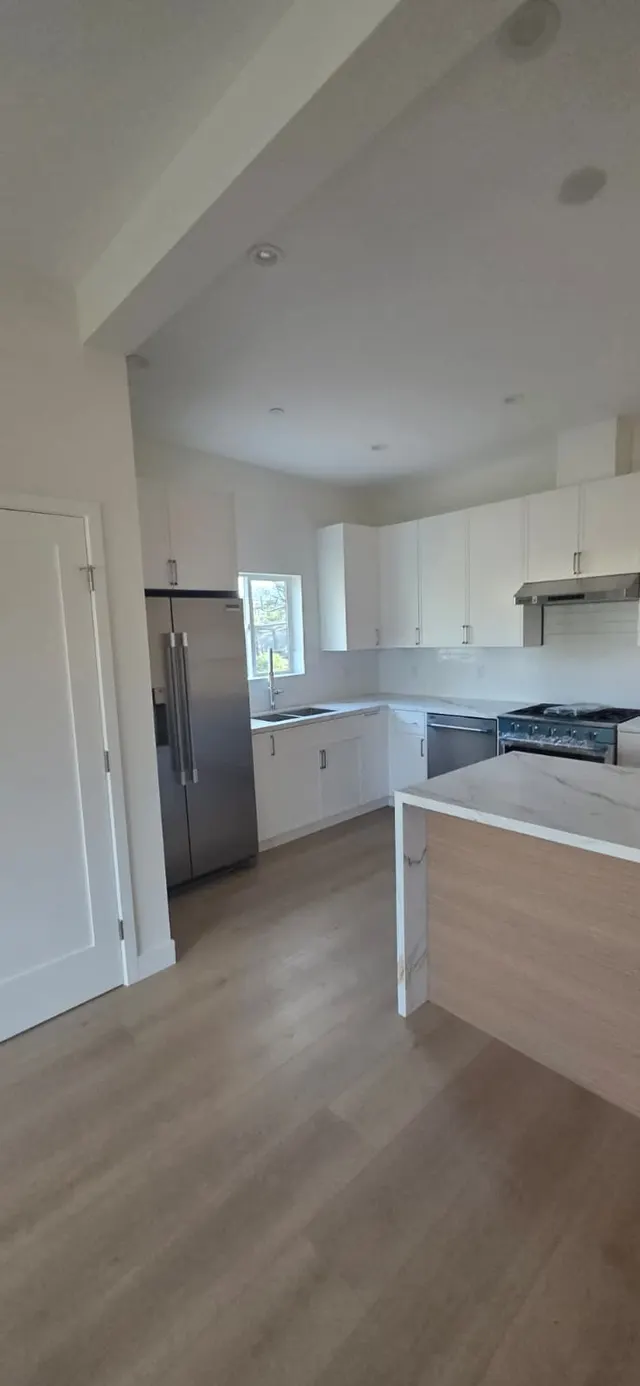 Stainless refrigerator, gas range, and dishwasher along the kitchen's white cabinet run