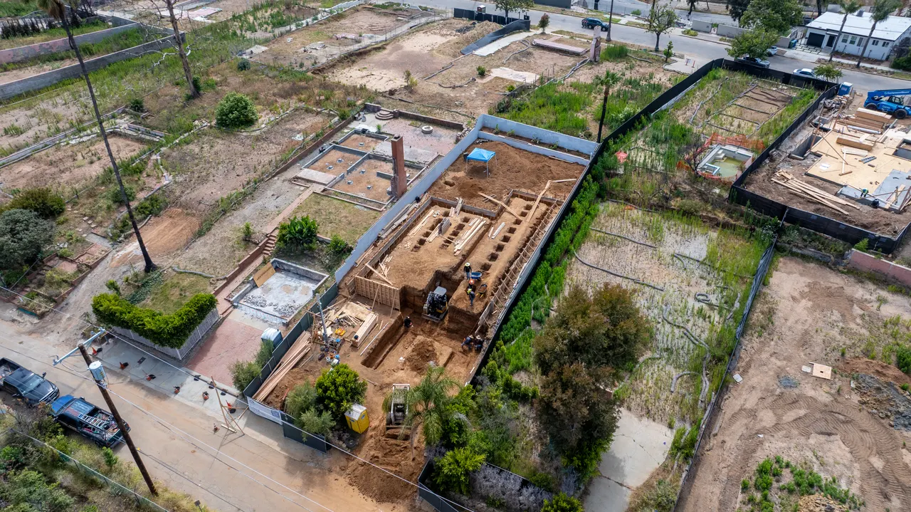 Aerial view of the lot within the surrounding block, showing the poured foundation walls alongside neighboring properties in various stages of construction