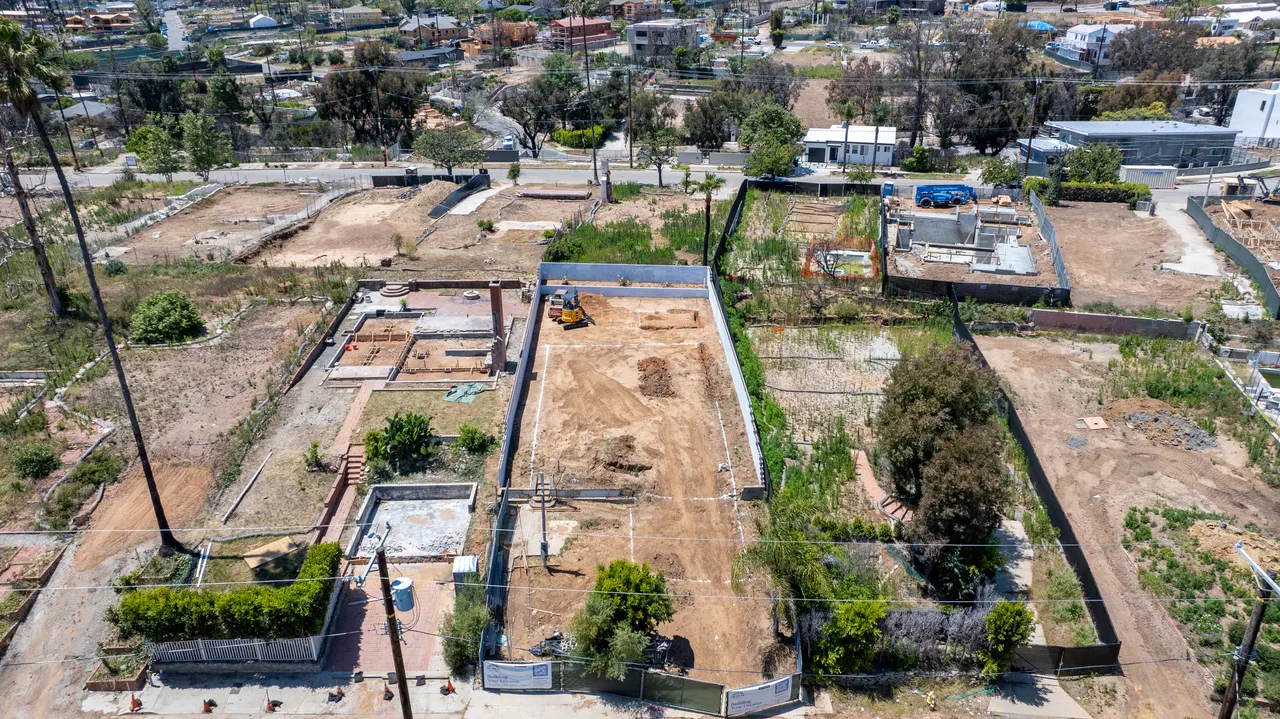 Earlier aerial view of the lot with the concrete retaining wall freshly poured and foundation excavation just getting underway