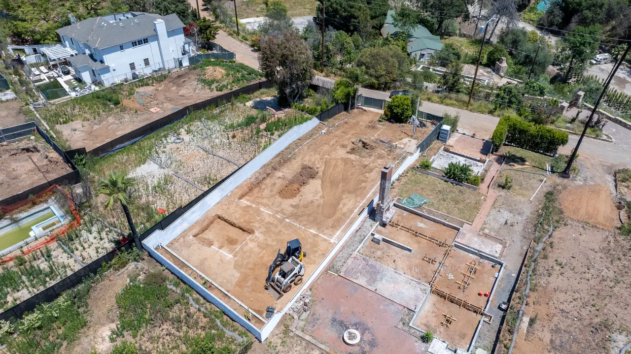 Aerial view of the poured foundation walls and graded pad, with a second foundation structure taking shape on the adjoining lot
