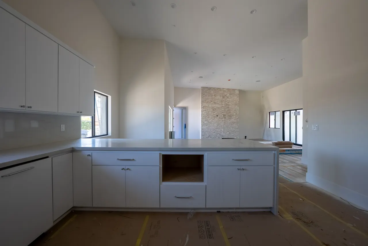Open-concept kitchen and great room with a floor-to-ceiling stacked-stone fireplace wall beyond the island, under a vaulted ceiling