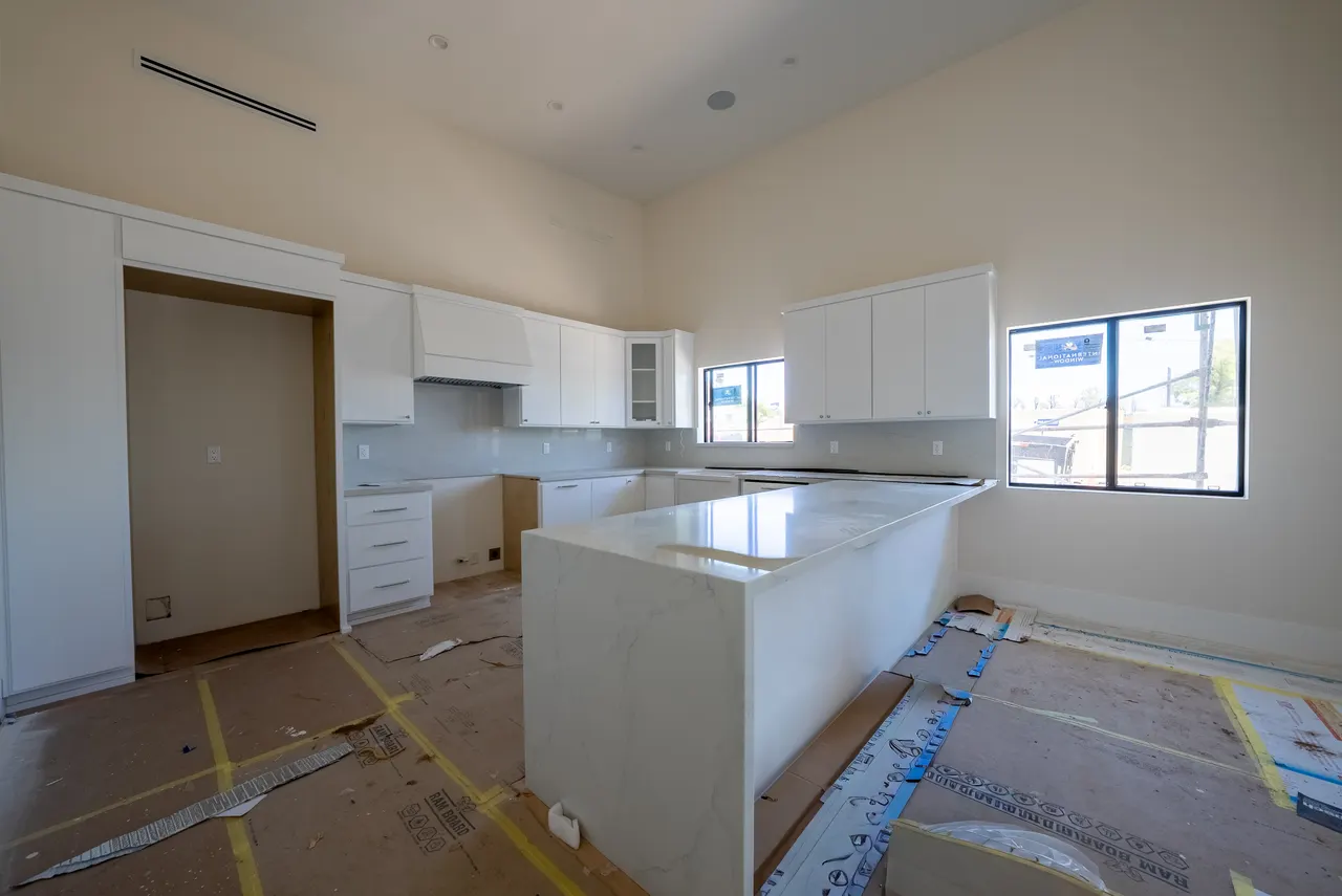 Kitchen island and marble-look backsplash with tall windows and white cabinetry; floor protection still down