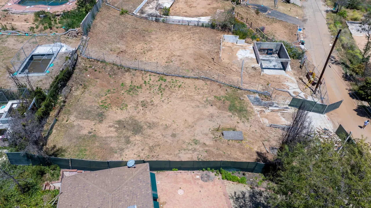 Aerial detail of a small in-ground utility structure staked out on the dirt lot near the property's edge, marking early site layout