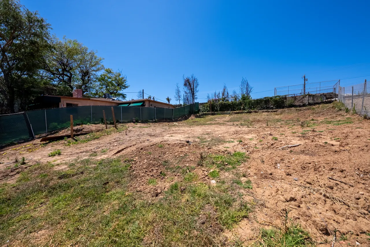 Ground-level view of graded dirt sloping toward a green construction fence line at the edge of the property