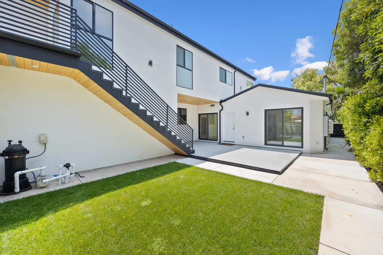 Backyard with an artificial turf lawn, concrete patio, and an exterior staircase leading to the upper-level unit