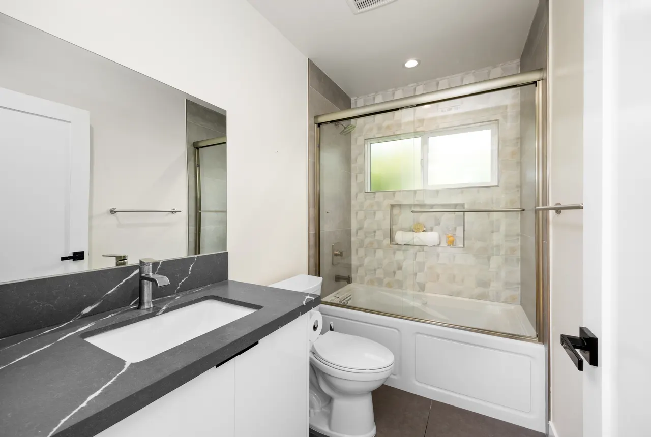 Bathroom with a dark stone-look vanity countertop, single sink, and a glass-enclosed tub-shower with patterned tile surround