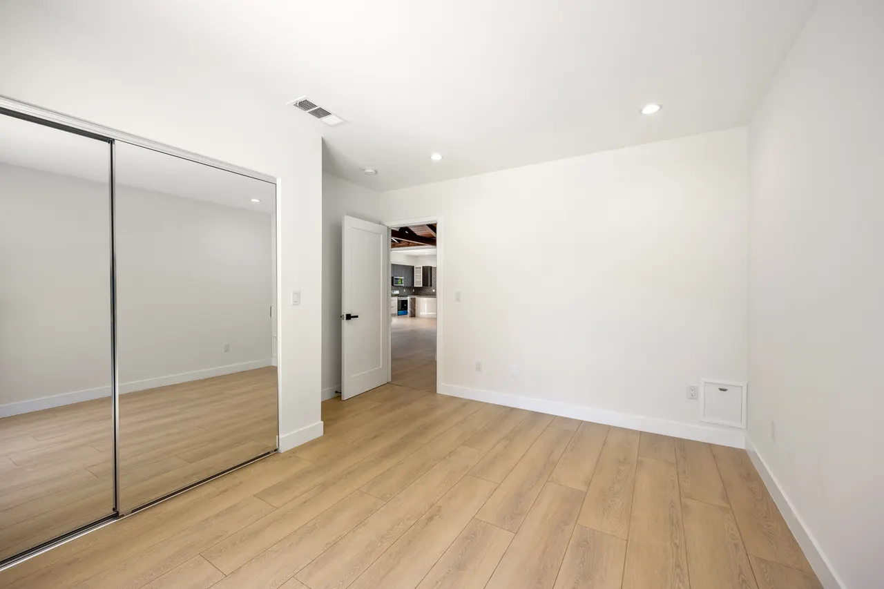 Bedroom with a full-width mirrored sliding closet door and light wood flooring, opening to a hallway