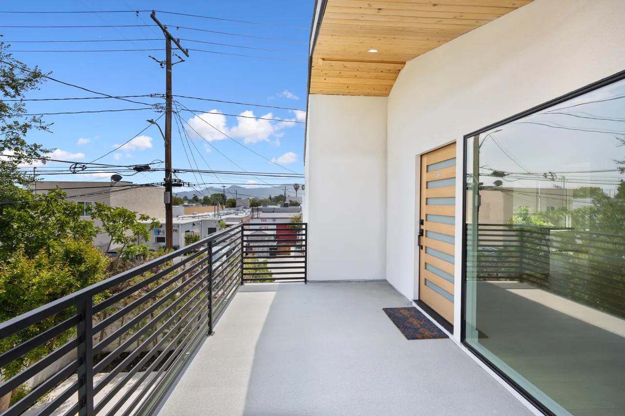 Covered upper-level deck with a tongue-and-groove wood ceiling, a glass sliding door, and a horizontal metal railing overlooking trees and distant hills