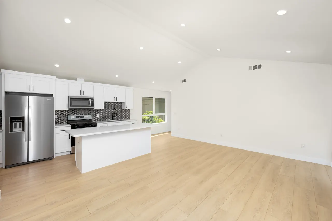 Open kitchen with white cabinetry, stainless steel refrigerator and range, a center island, and a vaulted ceiling opening to the living area