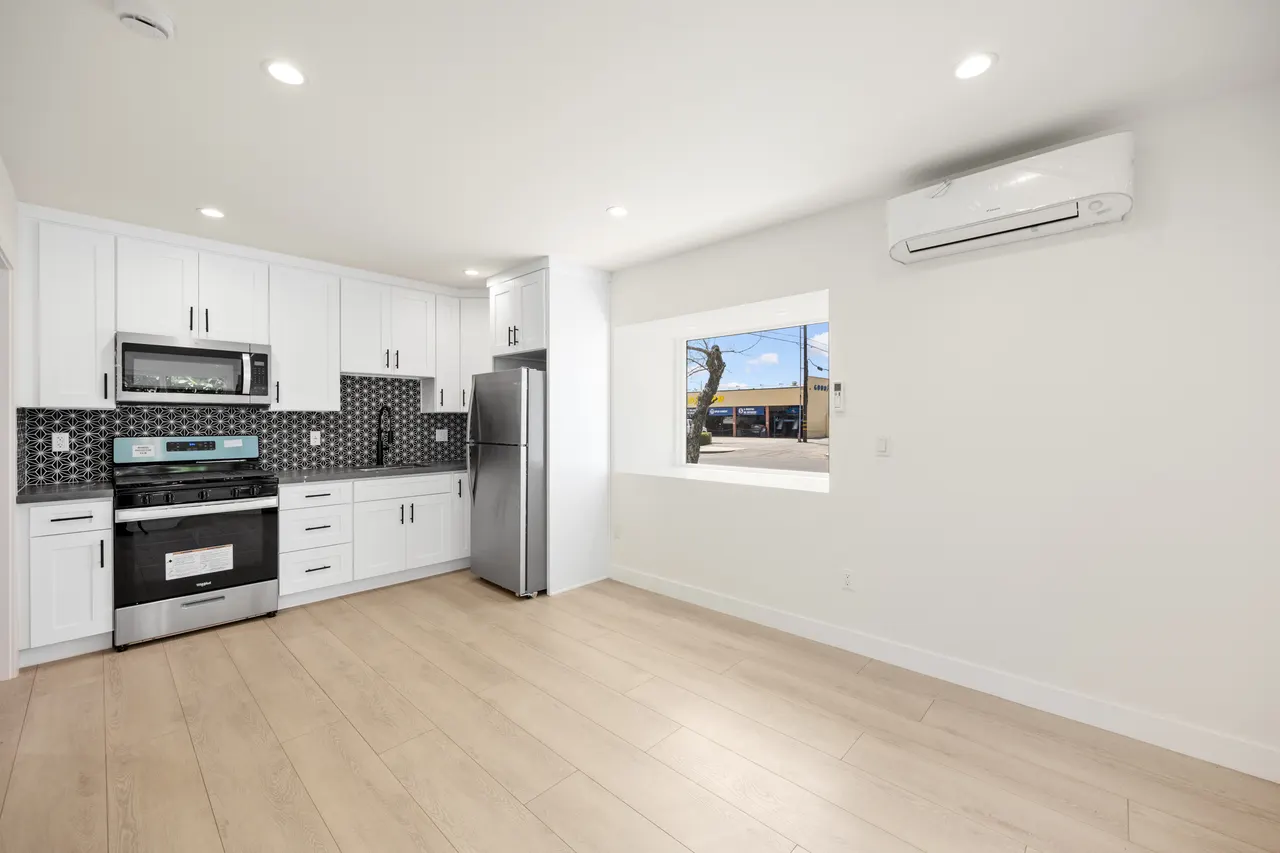 Kitchen with white shaker cabinetry, black countertops, star-patterned tile backsplash, and a stainless steel refrigerator and range