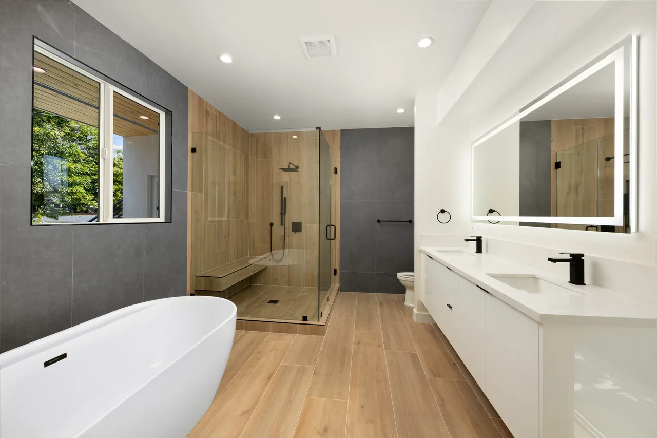 Primary bathroom with a freestanding soaking tub, a glass-enclosed walk-in shower with wood-look tile, and a white dual-sink vanity