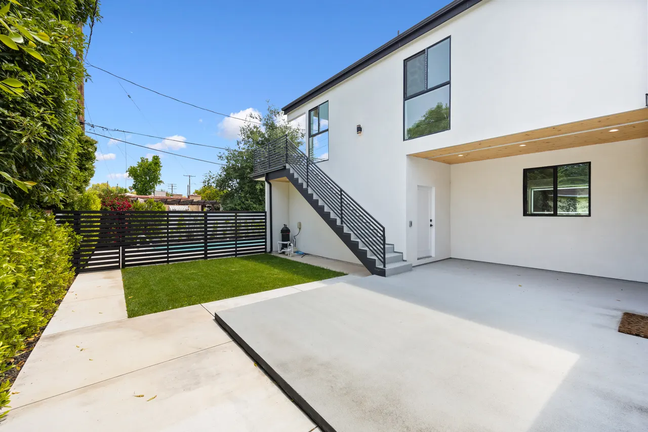 Exterior black metal staircase leading to a second-story unit, alongside a white stucco wall and concrete patio