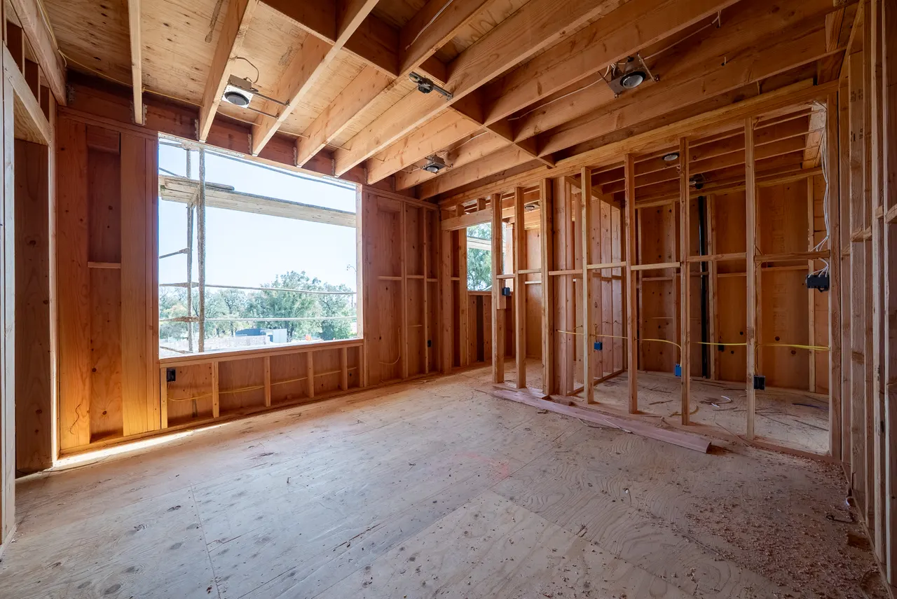 Wood-framed room with vaulted ceiling and a large window opening onto scaffolding and treetops