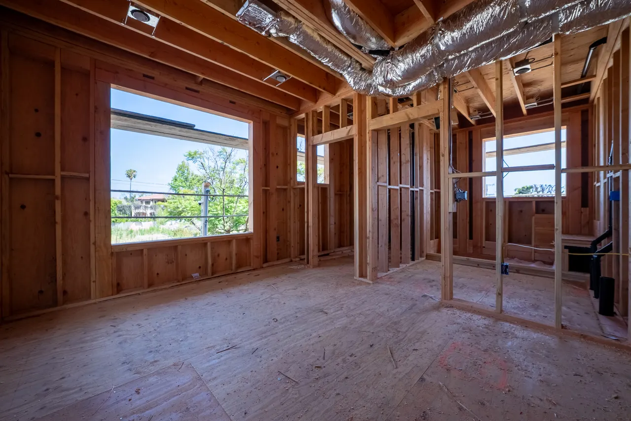 Framed great room with a picture window facing the yard and overhead HVAC ductwork roughed in