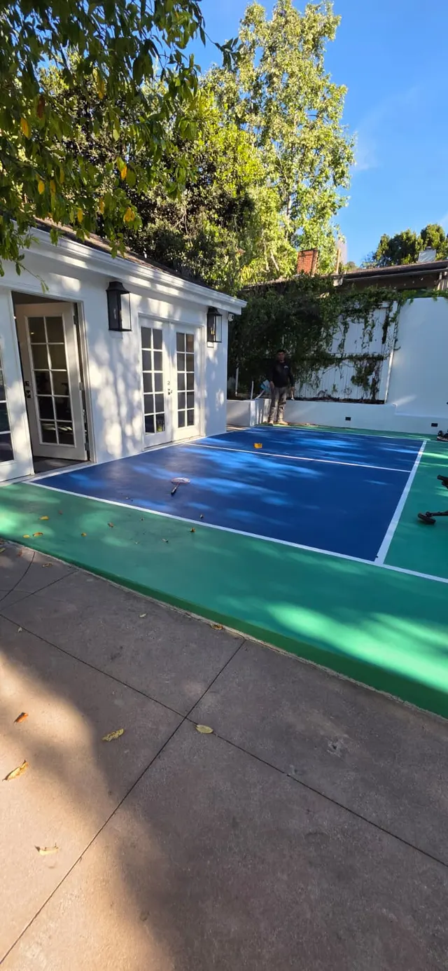 Finished blue-and-green sport court beside a white pool house with French doors and black wall sconces