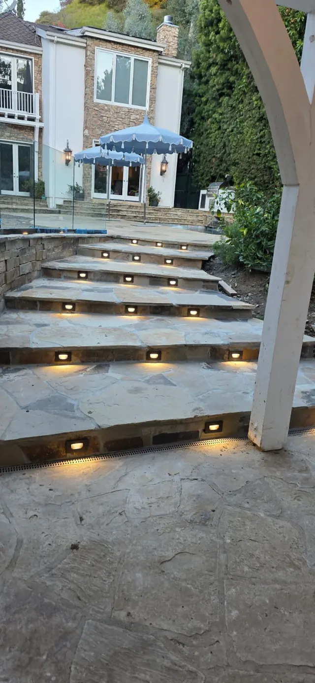 Close view of uplit flagstone stairs with recessed step lights, a glass railing, and a blue patio umbrella at the top